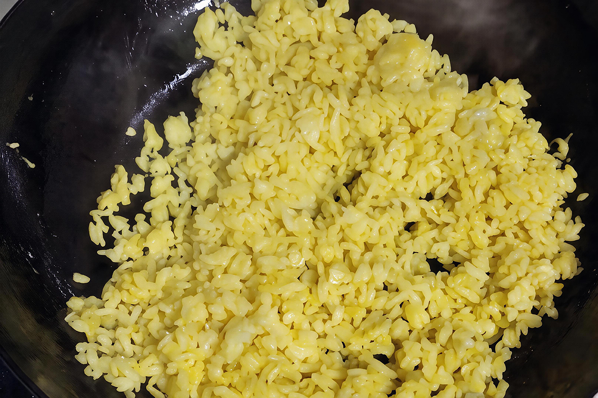 Egg-yolk-coated rice grains being stir-fried until golden and separated in a wok