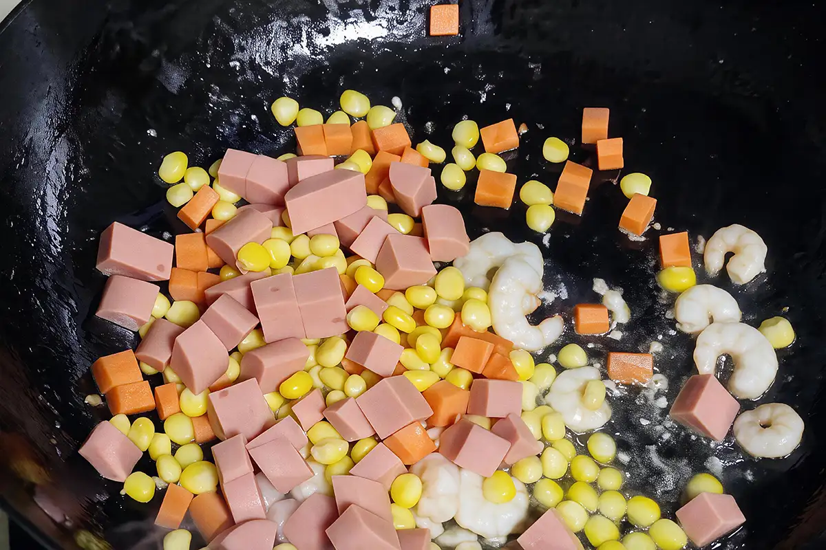 Stir-frying diced ham, corn, carrots, and shrimp together in a black wok