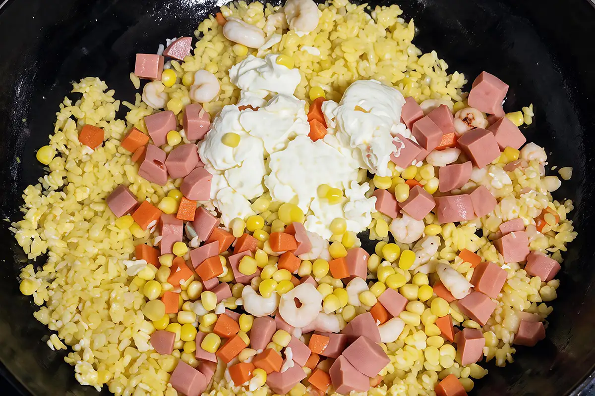 Returning ham, shrimp, corn, carrots, and egg whites to the wok with the fried rice