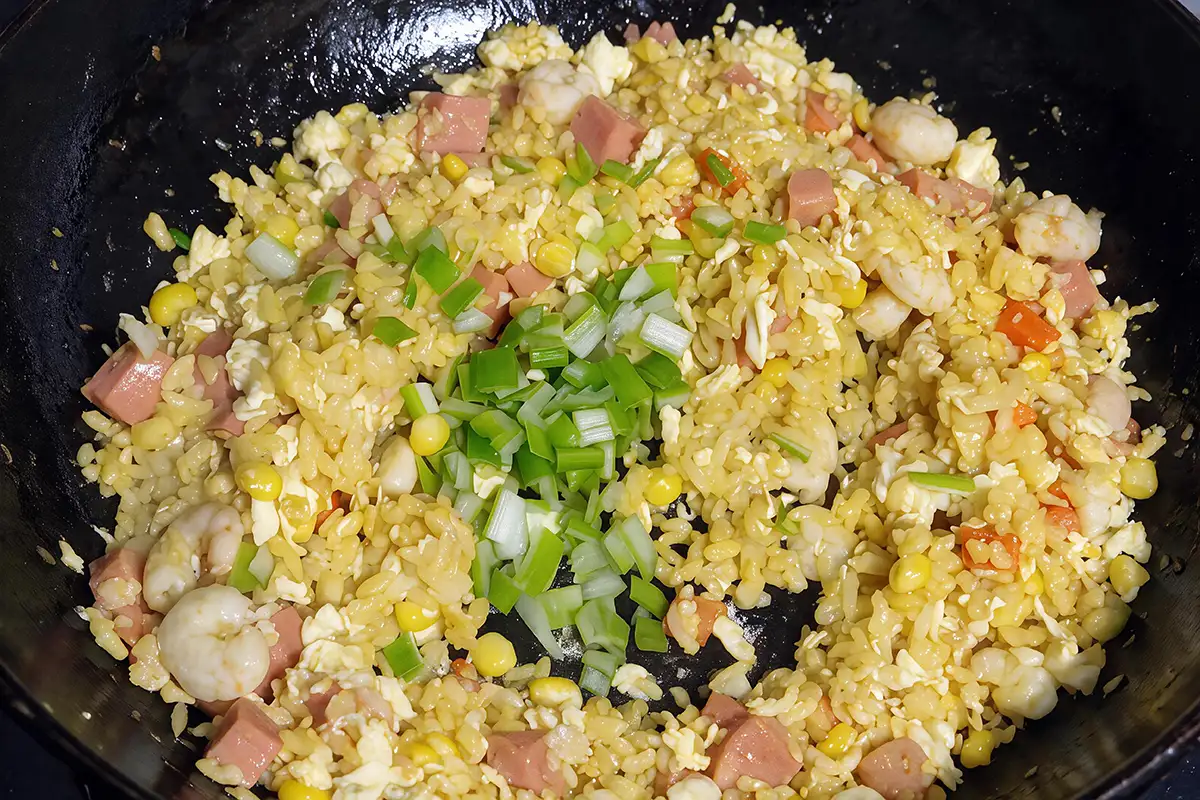 Finished Yangzhou fried rice in the wok topped with a mound of chopped green scallions