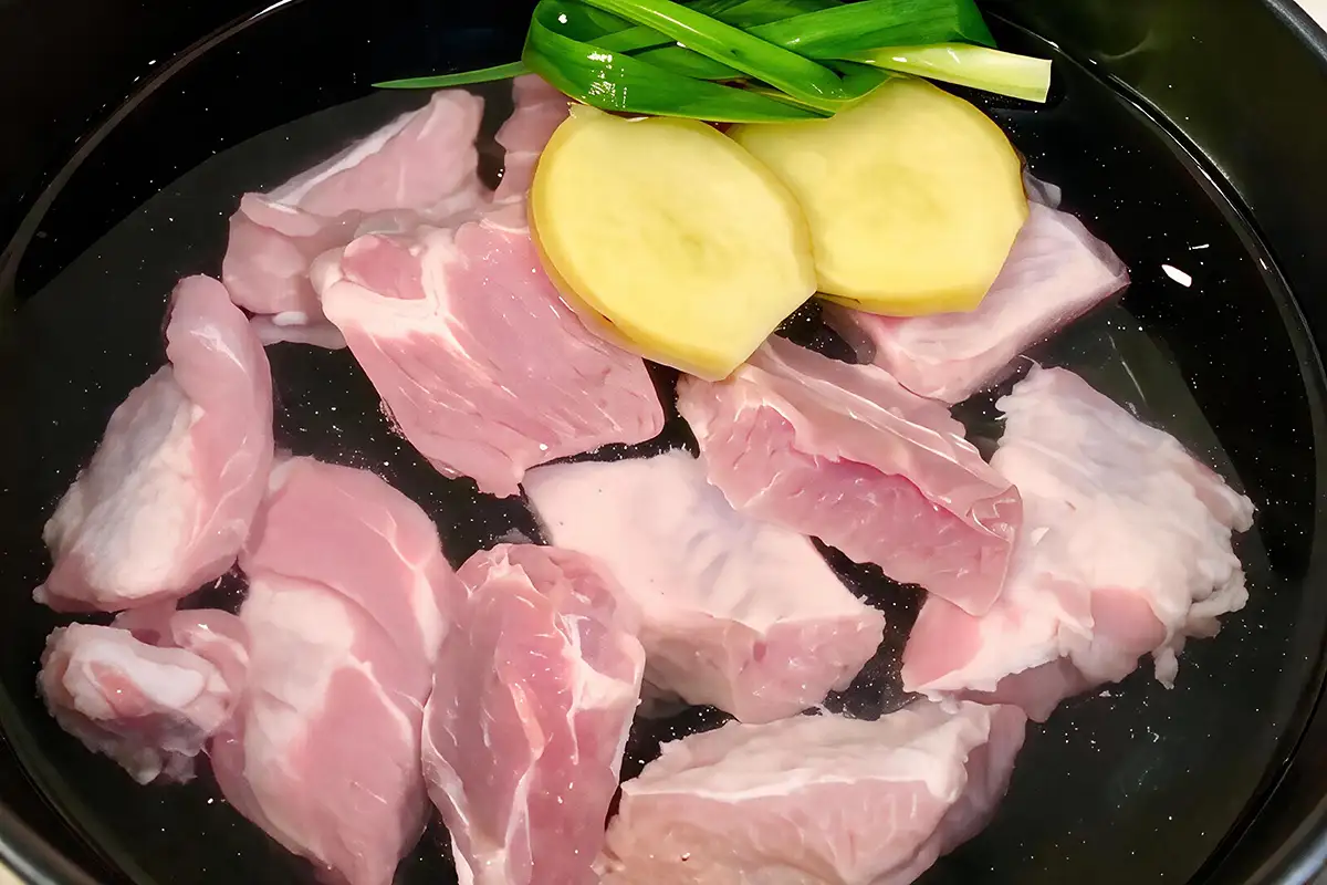 Raw pork ribs in cold water with ginger slices and scallion, ready to blanch