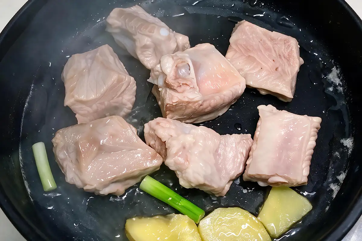Stir-frying blanched pork ribs with ginger and scallion until the edges turn light golden