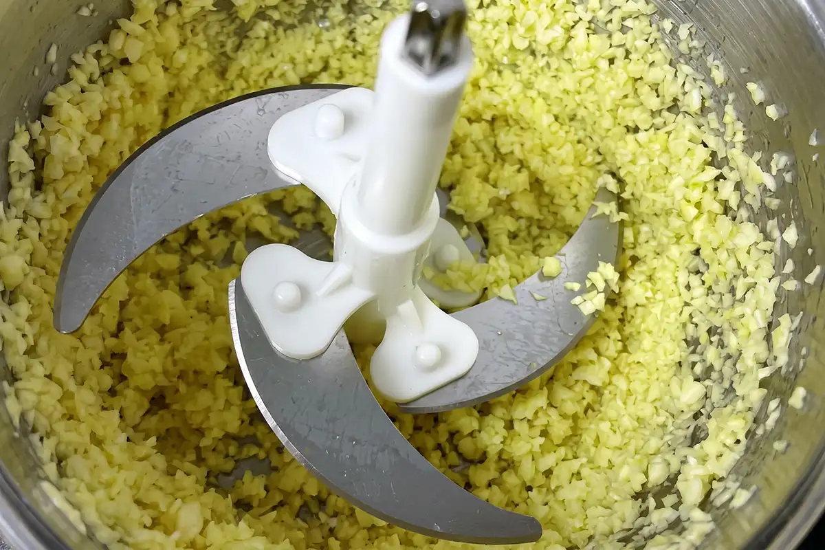 Coarsely minced garlic filling a food processor bowl with stainless steel blades