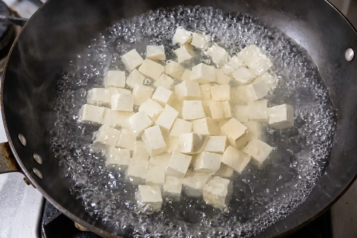 Cubed white tofu blanching in rapidly boiling water in a dark wok