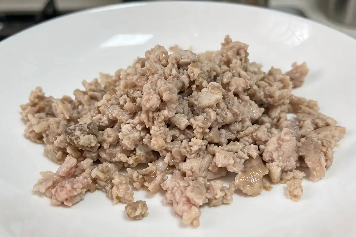 Cooked crumbled ground beef piled on a white plate after stir-frying until the edges crisp