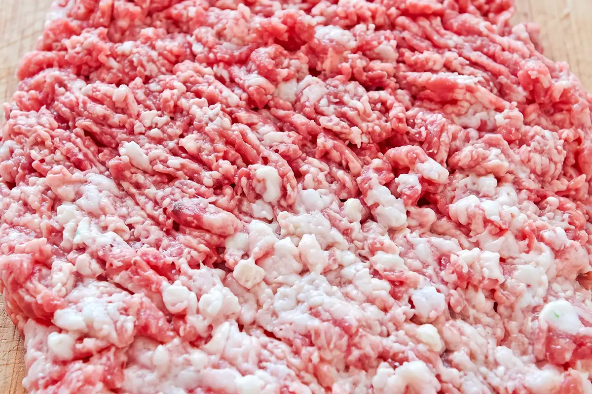 Hand-chopped pork shoulder and belly with visible lean and fat pieces on a wooden cutting board