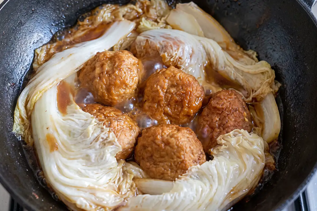 Five lion's head meatballs braising on napa cabbage leaves in a black wok with clear brown broth