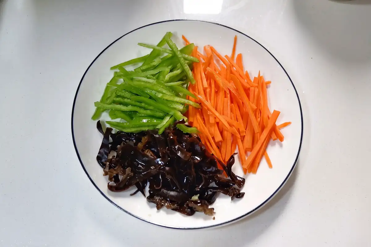 Shredded green bell pepper, carrot, and wood ear mushrooms arranged in separate piles on a white plate