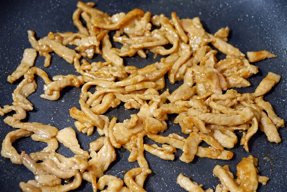 Marinated pork strips spread in a single layer and stir-frying in a hot wok
