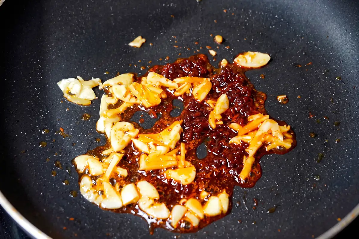 Doubanjiang, minced garlic, and ginger frying in oil until red oil releases in a wok
