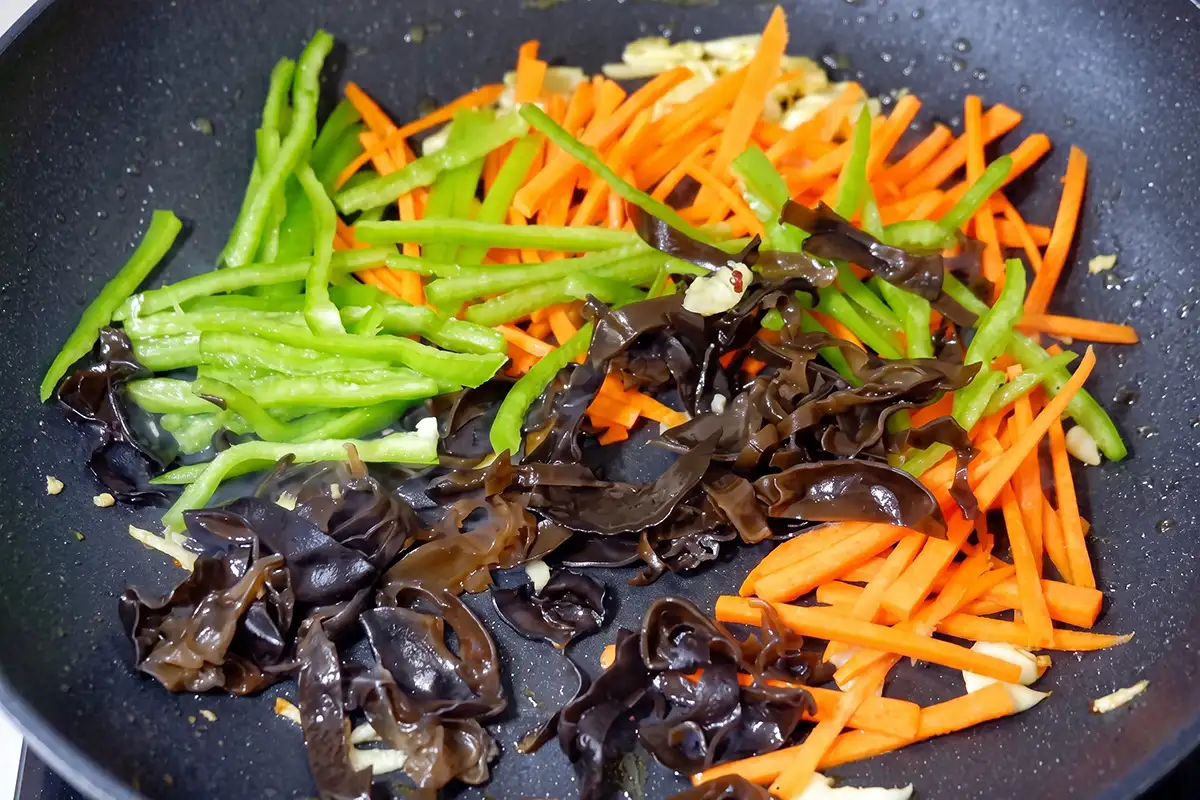 Shredded carrot, green bell pepper, and wood ear mushrooms stir-frying until tender-crisp in a wok