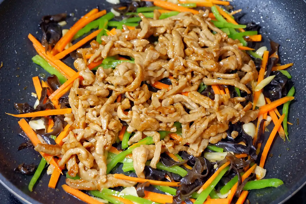 Pork returned to the wok with vegetables as pre-mixed Yu Xiang sauce is poured around the edge